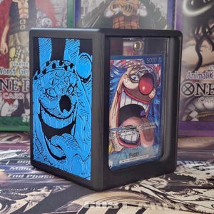 May include: Black display case with a clear front, displaying a trading card of a cartoon clown with a red nose and open mouth. The case has a blue embossed design on the side. The card reads "Buggy".