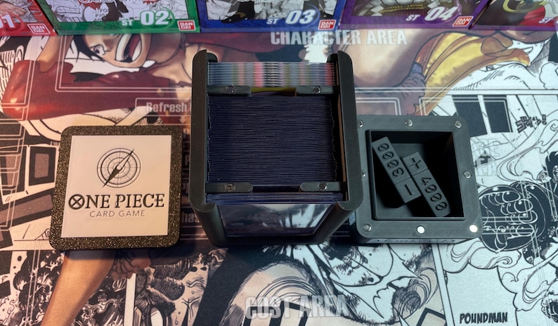 May include: A black card game box with a clear plastic lid, showing a deck of cards inside. The box has a label that says "One Piece Card Game". There is a separate black box with a compartment for dice.