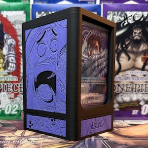 May include: Black card storage box with purple embossed artwork of a screaming face and other characters. The box holds a card with a character image. The word "Enel" is on the front of the box. Other card game boxes are in the background.