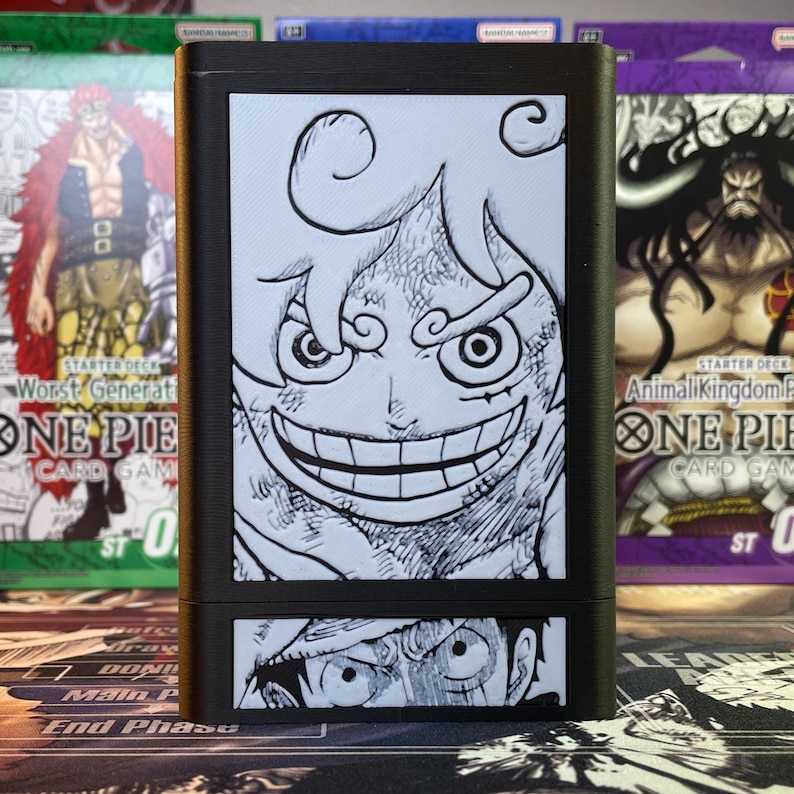 May include: A black card deck box with a white and black illustration of a character from the anime One Piece. The box has a black background with a white border. The illustration is of a character with a large grin and a scar on their face. The box is labeled "One Piece Card Game" and "Starter Deck".