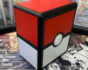 May include: A red, white, and black card storage box with a design resembling a Poké Ball. The box has a red top, a white bottom section, and a black border. A white circle with a smaller white button is centered on the front. The box is designed to hold trading cards.