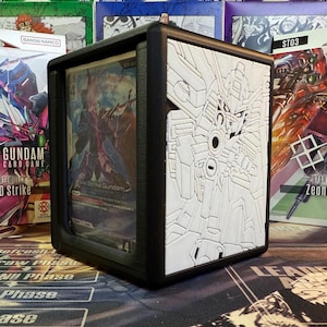 Puede incluir: Estuche de cartas negro con un diseño Gundam en relieve blanco. El estuche contiene una carta de Gundam con una ilustración colorida. El estuche está diseñado para proteger y exhibir cartas coleccionables.