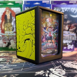 May include: A black card holder with a yellow embossed design on the side. The front displays a colourful card featuring a character named Vegapunk. The card holder is designed to protect and showcase trading cards.
