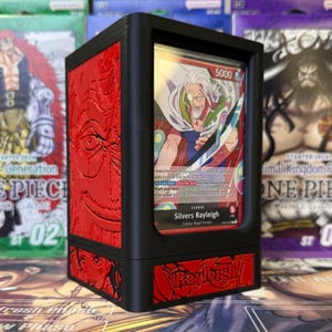 May include: Black and red card holder featuring a card with the text "Silvers Rayleigh". The holder has a black frame with red embossed detailing and the name "Rayleigh". Other card game boxes are in the background.