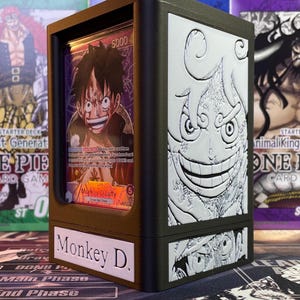 May include: A brown and black wooden card game deck box with a clear plastic window showing a card with an illustration of Monkey D. Luffy. The box has a white label on the front that says "Monkey D."