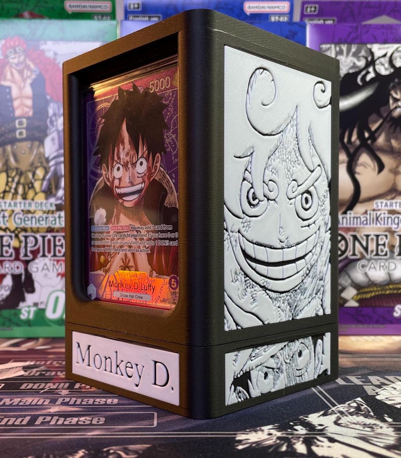 May include: A brown and black wooden card game deck box with a clear plastic window showing a card with an illustration of Monkey D. Luffy. The box has a white label on the front that says "Monkey D."