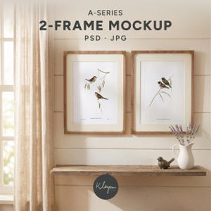 Könnte beinhalten: A-SERIES 2-FRAME MOCKUP PSD JPG. Zwei vertikale Holzrahmen mit weißen Passepartouts und Vogelillustrationen hängen an einer horizontalen Wandverkleidung über einem Holzregal. Ein weißer Keramikkrug mit getrocknetem Lavendel und eine kleine Vogelfigur stehen auf dem Regal.