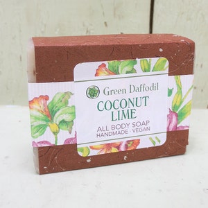 May include: A brown cardboard box with a white label that reads "Green Daffodil Coconut Lime All Body Soap Handmade - Vegan". The label has a floral design with yellow, orange, and pink flowers.