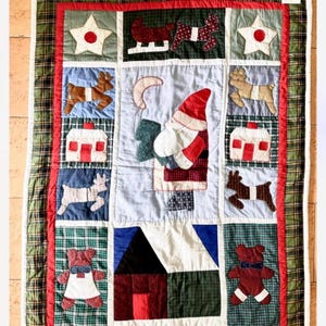 Könnte beinhalten: Eine Patchwork-Decke mit Weihnachtsmotiv. Die Decke zeigt verschiedene Weihnachtsmotive, darunter den Weihnachtsmann, Rentiere, Häuser und Sterne. Die Decke ist aus verschiedenen Stoffen in Rot, Grün, Blau und Weiß gefertigt.