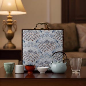 May include: A tea set with a light blue teapot, various cups, and a patterned box. The box has a handle and a blue, white, and red wave design. The set includes a clear glass and a small, red-orange cup.