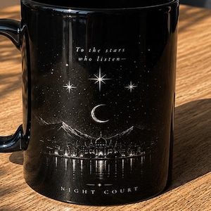 Op de afbeelding: Een zwarte keramische mok met een witte afbeelding van een berglandschap, een maansikkel en sterren. De tekst "To the stars who listen-" staat boven de illustratie en "NIGHT COURT" onderaan, met een handvat aan de linkerkant van de mok.