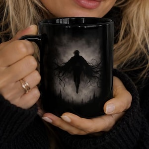May include: A black ceramic mug featuring a dark, atmospheric graphic print of a silhouetted figure with long, flowing, tentacle-like appendages floating above a misty forest landscape. The design is centered on the front of the glossy black mug.