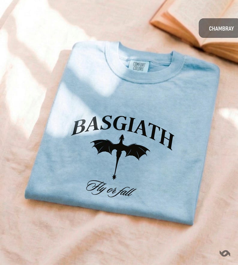 Peut inclure: T-shirt bleu clair avec le mot "BASGIATH" en arc de cercle et un dessin de dragon noir en dessous. L'inscription "Fly or fall" est imprim&eacute;e en dessous. Marque Comfort Colors.