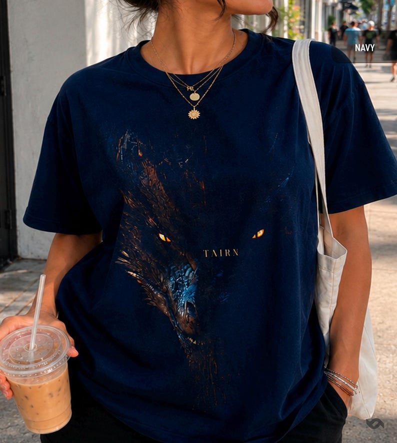 May include: Navy blue t-shirt featuring a detailed graphic of a wolf's face with glowing yellow eyes. The word "TAIRN" is printed below the image. The shirt is short-sleeved and made of a soft material.