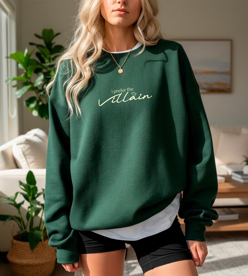 May include: A dark green sweatshirt with the text "I prefer the villain" in a cursive font. The sweatshirt has a white collar and is worn with black shorts. The overall style is casual and comfortable.
