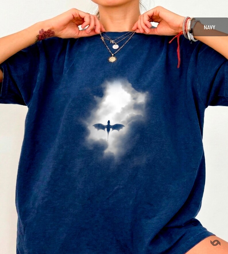 May include: Navy blue t-shirt featuring a dragon silhouette against a cloudy sky. The graphic is centered on the shirt. The shirt has short sleeves and a relaxed fit. The word "NAVY" is in the upper right corner.