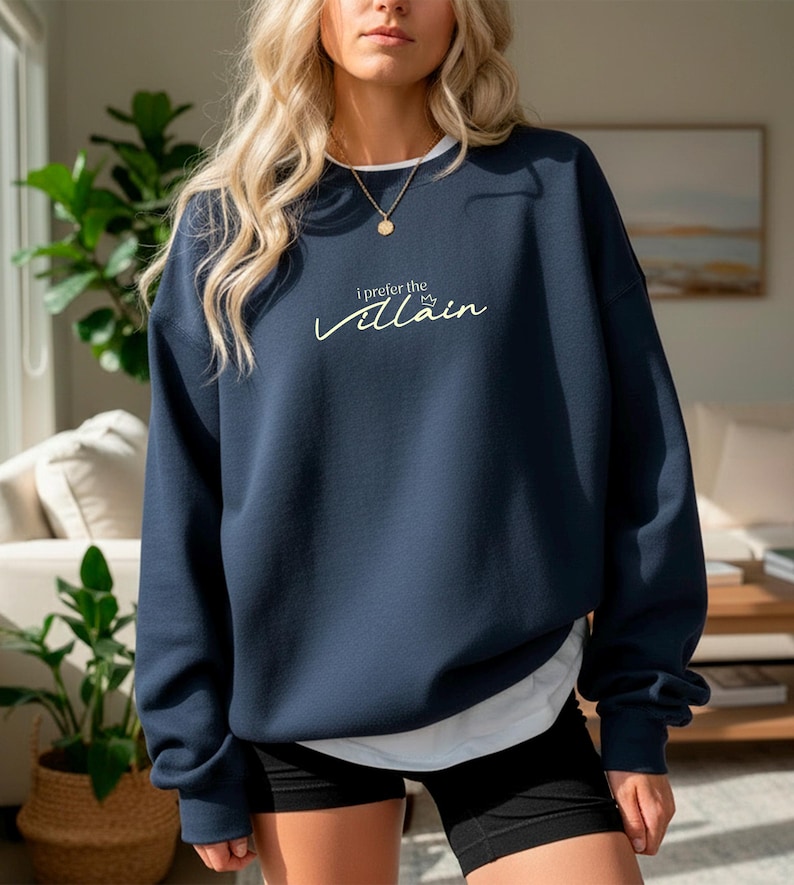 May include: Navy blue sweatshirt with the text "I prefer the Villain" in a cursive font. The sweatshirt has a white collar and is worn with black shorts. A gold necklace is visible.