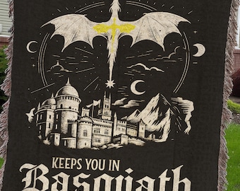 May include: Black woven throw blanket with a fantasy design. Features a dragon, castle, and the text "A Book A Day Keeps You In Basgiath" in a gothic font. Edges have a fringed trim.