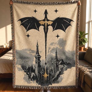 Può includere: Una coperta tessuta che presenta la sagoma di un grande drago nero e oro che vola sopra un'illustrazione dettagliata di un castello grigio e bianco. Il design include quattro stelle a quattro punte e frange sui bordi superiore e inferiore.