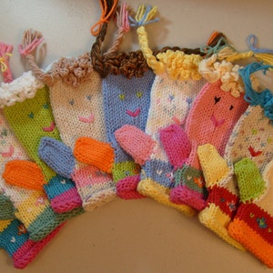 Op de afbeelding: Een verzameling van tien gebreide vingerpoppen met kleurrijk garen en lachende gezichten. Elke pop heeft een andere kleur en ontwerp, waaronder roze, blauw, groen, geel en oranje.