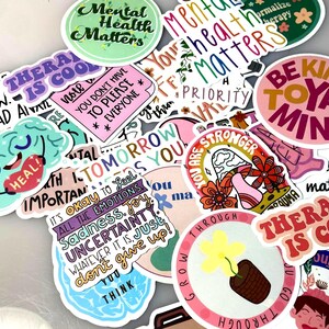 May include: A collection of colorful stickers with various motivational and mental health-related phrases. The stickers feature text like "Mental Health Matters," "Therapy is Cool," and "Be Kind to Your Mind," along with floral and brain illustrations.