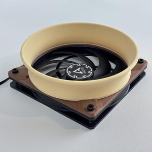 May include: A computer fan with a black fan blade and a beige-colored shroud. The fan is mounted on a brown and black square frame. The center of the fan has the word "ARCTIC" printed on it.
