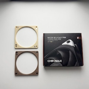 Puede incluir: Una caja de producto negra etiquetada Noctua NF-A12x25 PWM chromax.black.swap con un gráfico de un ventilador de computadora, acompañada de dos marcos de ventilador cuadrados en beige y marrón, cada uno con cuatro puntos de montaje magnéticos.
