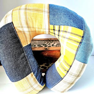 May include: A patchwork travel pillow in a U-shape, featuring denim, yellow plaid, and cream-colored fabric. The pillow is designed for neck support and comfort, with a central opening. The fabrics are sewn together in a geometric pattern.