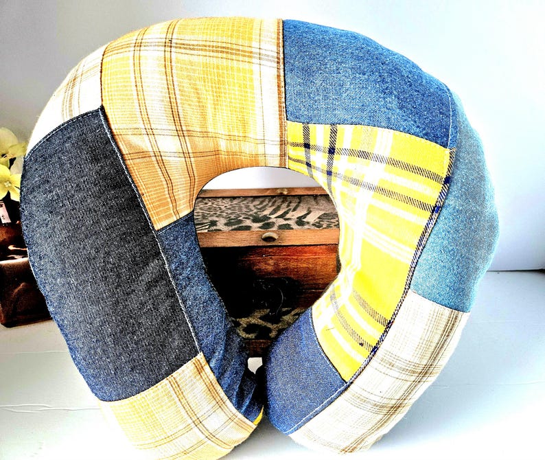 May include: A patchwork travel pillow in a U-shape, featuring denim, yellow plaid, and cream-colored fabric. The pillow is designed for neck support and comfort, with a central opening. The fabrics are sewn together in a geometric pattern.