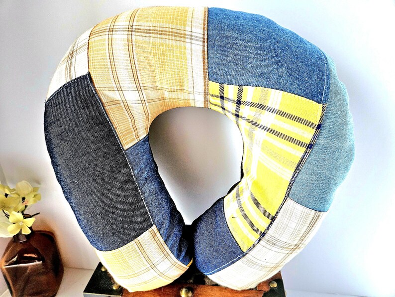 May include: A patchwork travel pillow in a U-shape, featuring denim, yellow plaid, and gray fabric sections. The pillow is designed for neck support and comfort, with a central opening. The color palette includes blue, yellow, and gray.