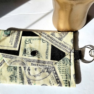 May include: A small black and white fabric pouch with a zipper closure and a key ring. The pouch is printed with images of US dollar bills.
