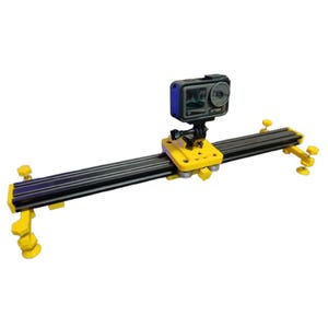May include: A black and yellow camera slider with a black action camera mounted on top. The slider has adjustable legs and a smooth track for filming.