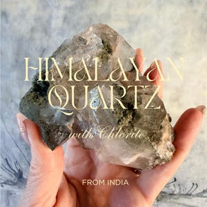 May include: A cluster of Himalayan quartz with green chlorite inclusions. The crystal features translucent, jagged points and a textured, earthy base. Text overlay reads: HIMALAYAN QUARTZ with Chlorite FROM INDIA. The specimen displays natural facets.