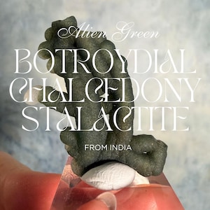 May include: A dark green botryoidal chalcedony stalactite from India. The image features the text "Alien Green" and the words "BOTROYDIAL CHALCEDONY STALACTITE" in a white, elegant font. The stalactite is held in a person's hand.
