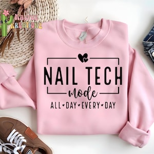 Puede incluir: Sudadera rosa claro con el texto negro "NAIL TECH mode ALL DAY EVERY DAY". La sudadera está doblada, con zapatillas marrones y vaqueros azules visibles. Un logotipo de cactus está en la esquina superior izquierda.