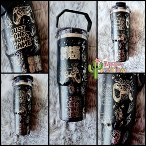 May include: Black and gold gamer themed tumbler with a handle. The tumbler has a variety of graphics including a game controller, lightning bolts, and the text "Game Over", "Eat Sleep Game Repeat", and "Just One More Game".