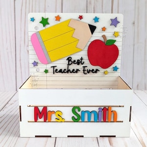 May include: White wooden box with a pencil, apple, and stars on the lid. The box has the text "Best Teacher Ever" and "Mrs. Smith" on it.