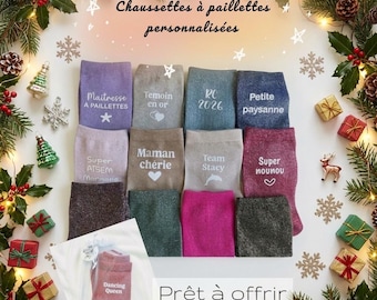 May include: A collection of twelve pairs of glittery socks in various colors including purple, gray, blue, brown, pink, and black. Each pair features custom white text and symbols such as hearts, stars, and a dolphin. One pair is shown packaged in a clear bag.