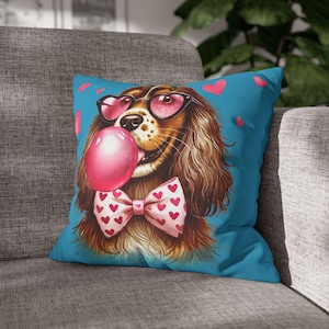 Könnte beinhalten: Ein blaues Kissen mit einem braunen und weißen Hund, der eine rosafarbene Herz-Sonnenbrille und eine rosafarbene Fliege trägt. Der Hund bläst eine rosafarbene Blase.