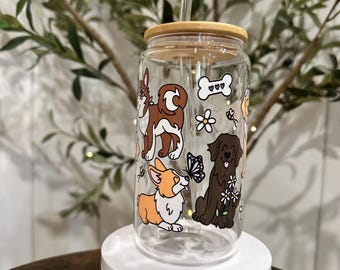 May include: Clear glass reusable water bottle with a bamboo lid and a straw. The bottle features a colourful illustration of four dogs with flowers and a butterfly.