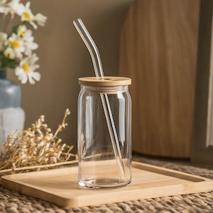 May include: A clear glass drinking jar with a bamboo lid and a glass straw. The jar is sitting on a wooden tray.