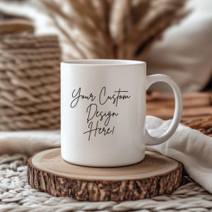 May include: White ceramic mug with a curved handle, featuring the text "Your Custom Design Here!" in black script. The mug is displayed on a round, natural wood slice, with a blurred background.