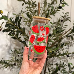 Op de afbeelding: Een heldere glazen beker met een bamboe deksel en een helder rietje. De beker is versierd met rode watermeloen schijfjes, bloemen en hartjes. De beker is ongeveer 15 cm hoog.