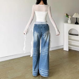 Women's Asymmetrical Mesh Tops | Long Sleeve Patchwork Shirt | Streetwear Y2k Chic Fashion

A fitted long sleeve top with cascading ribbon-like drapes extending at the sides, worn with wide-leg jeans. The piece has a structured upper silhouette and flowing layered accents for a dramatic, fashion-forward look.