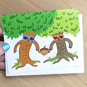 Puede incluir: Tarjeta de felicitación con una ilustración de dos árboles antropomórficos con gafas de sol, tomados de la mano de una bellota sonriente. Los árboles son marrones y naranjas con hojas verdes, sobre un fondo blanco.
