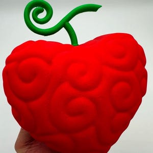 May include: A red 3D printed fruit with a green stem and swirl design. The fruit is shaped like a heart and has a textured surface.
