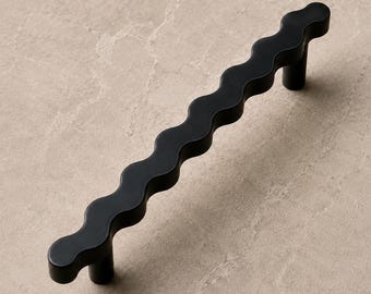 May include: A matte black cabinet handle featuring a distinct wavy, serpentine silhouette. The hardware has a continuous undulating form with two cylindrical mounting posts positioned at each end to secure the handle to a flat surface.