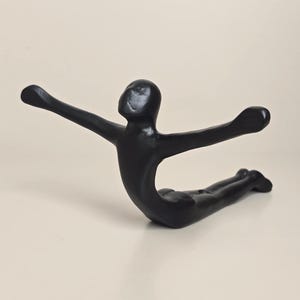 May include: A black sculpture of a person in a yoga pose, with arms outstretched. The figure is lying on its stomach with legs extended. The sculpture has a smooth, glossy finish and is set against a neutral background.