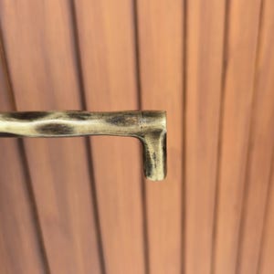 May include: A close-up of a gold-colored metal handle with a textured surface. The handle has a right-angled, L-shaped design. The background is a series of vertical, wooden planks.