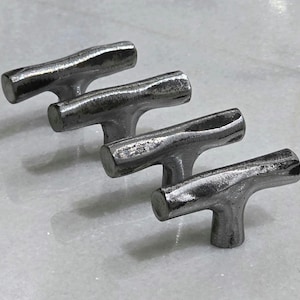 May include: Four silver-toned metal cabinet pulls with a T-shaped design. The pulls have a textured, rustic appearance and are arranged in a diagonal row. These hardware pieces are suitable for drawers or cabinets.